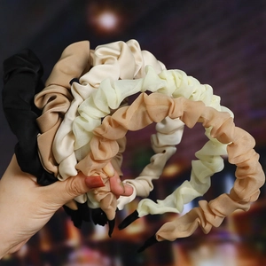 Close-up of pleated fabric headbands in black, beige, cream, and brown held by hand
