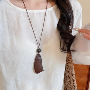 Detail of vintage wooden pendant necklace with textured wood seed on white linen shirt