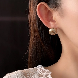 Close-up of elegant gold pearl stud earrings worn by a model with a minimalist aesthetic