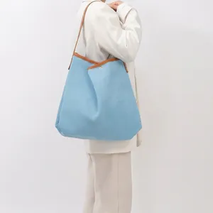 Detailed shot of large blue woven tote bag with brown leather straps on female model
