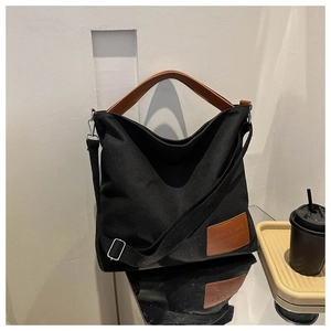 Detail of black canvas tote bag with brown leather handles and a fashion label on a table
