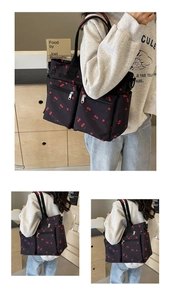 Detail of black tote bag with red cherry print featuring front zipper pockets and wide straps