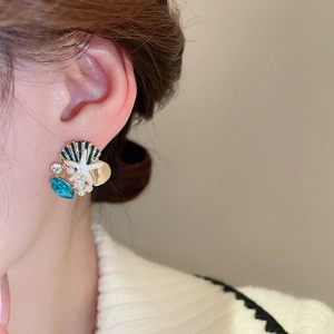 Close-up of ocean-themed earrings featuring a blue shell and starfish on a female model