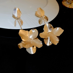 Detailed close-up of golden 3D flower tassel earrings on white plate with black background
