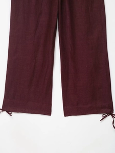 Detail view of deep burgundy linen trousers featuring adjustable drawstring cuffs and texture
