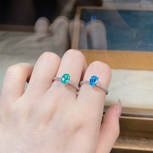 Detailed view of S925 silver rings with emerald green and blue gemstones on a model's hand