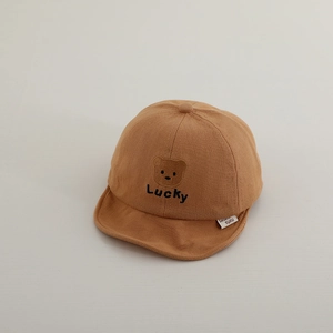 Detail of baby cotton cap featuring embroidered bear and lucky text on camel fabric