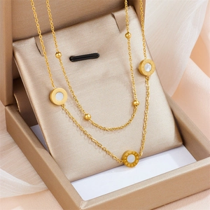 Double-layered gold Roman numeral necklace with shell pendant on a beige jewelry display