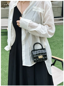 Outdoor shot of a black diamond-quilted jelly bag with gold chain strap on grass