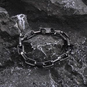 Detail of a black stainless steel box chain bracelet on a textured dark rock background