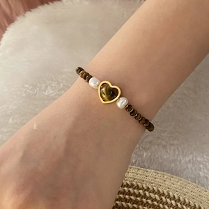 Detail of tiger eye bead bracelet with gold heart pendant and pearls on model wrist