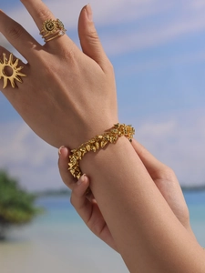 Close-up of gold spike bracelet and sun rings worn by a model at the beach