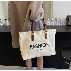 Nahaufnahme einer cremefarbenen Canvas-Tasche mit braunen Ledergriffen und schwarzer Aufschrift