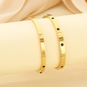 Detail of gold bracelets with black stones displayed on a beige silk textured background