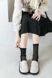 Detail of black mesh crew socks with ruffle trim styled with beige loafers for women