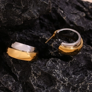 Macro shot of two-tone gold and silver C-shaped earrings on black volcanic stone
