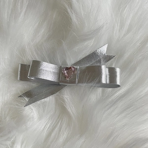 Detail of silver metallic bow hair clip with pink heart-shaped gemstone on white plush