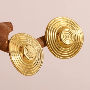 Detailed shot of 18K gold-plated concentric swirl earrings hanging on a wooden branch