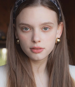 Close-up of golden spherical earrings worn with a dark vintage pattern headband