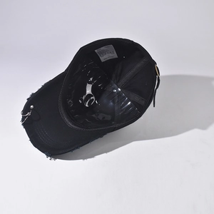 Detail showing distressed holes and decorative silver metal ring on a black cotton denim cap