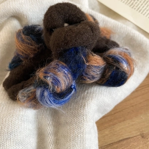 Close-up of fluffy multi-color velvet hair claw clip on soft white knit background