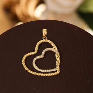 Détail macro du pendentif double cœur doré avec texture torsadée et cristaux pavés