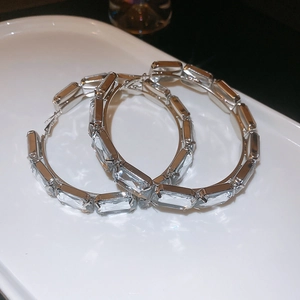 Close-up of large silver hoop earrings with rectangular cut clear crystals on white tray