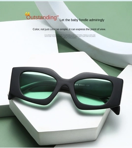 Detail of black cat-eye kids sunglasses with matte resin frame and green lenses on stone