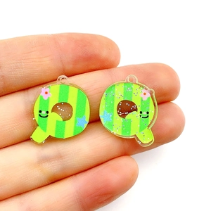 Macro shot of striped acrylic Q-letter charms with glitter finish on fingertips
