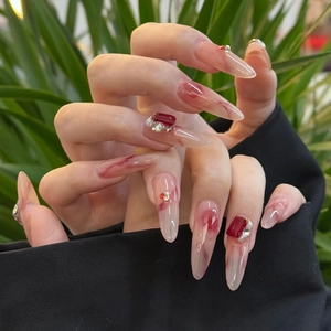 Détail de faux ongles amande avec motif marbre rouge, perles et bijoux en rubis