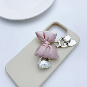 Detail of pink silk bow with silver heart pendants attached to a beige phone case