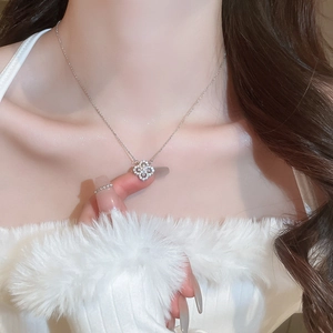 Detail of silver clover necklace with zircon inlay worn on neck in close-up view