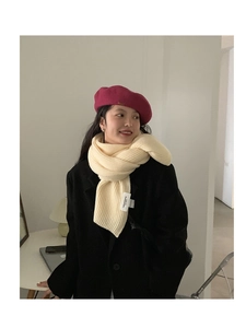 Detail of cream chunky knit ribbed scarf with white cloth label and red wool beret hat