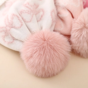 Close-up of soft pink jacquard knit texture and fluffy faux fur pom-pom on girls' winter hat