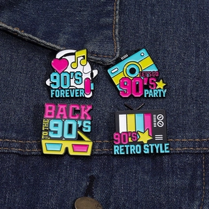 Gros plan de quatre pin's rétro des années 90 avec TV et caméra sur une veste en jean