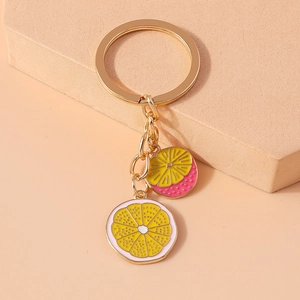 Close-up of yellow lemon and pink fruit slice keychains on a gold metal ring