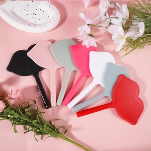 Lip-shaped handheld makeup mirrors in seven various colors on a decorative floral background