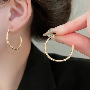 Macro detail of large gold-tone C-shape hoop earrings with high-polished metallic finish