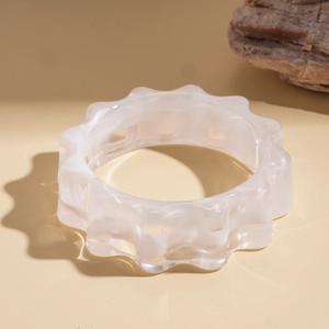 Dettaglio di bracciale in acrilico bianco ondulato su pietra con luce calda soffusa
