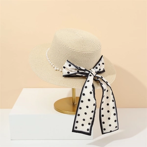 Beige flat top straw sun hat with white pearls and a black polka dot ribbon bow