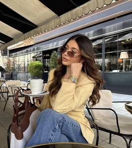 Detailaufnahme eines gelben Langarm-Blazers kombiniert mit Jeans in einem Outdoor-Café