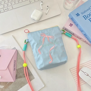 Détail du sac bandoulière en toile bleu clair avec broderie nœud rose et bandoulière