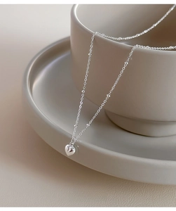 Detail of S925 sterling silver heart necklace hanging on a grey ceramic cup