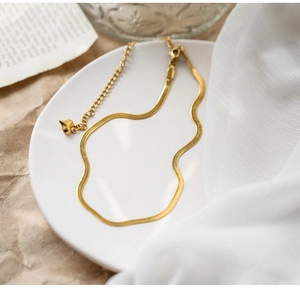 Detail of a golden herringbone chain with a heart-shaped pendant on a white ceramic plate