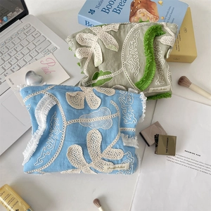 Detail of floral embroidery and fringe trim on blue and sage green makeup bags