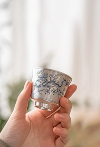 Primer plano de una mano sosteniendo una taza de té plateada con un dragón azul