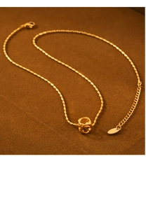 Detail shot of a gold hollow cube pendant on a beaded chain over brown suede material