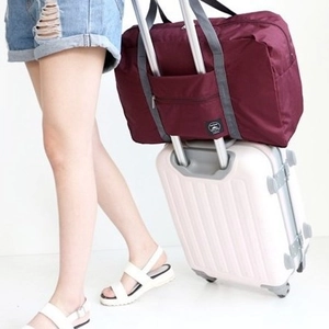 Foldable burgundy travel bag with luggage handle sleeve on a white suitcase