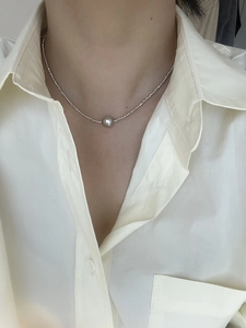 Detail of minimalist silver beaded necklace with round pearl pendant on neck