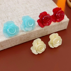 Détail de boucles d'oreilles rose en résine bleue, rouge et crème sur surface texturée